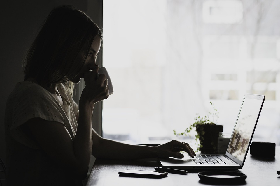 woman drinking coffee while typing on a laptop